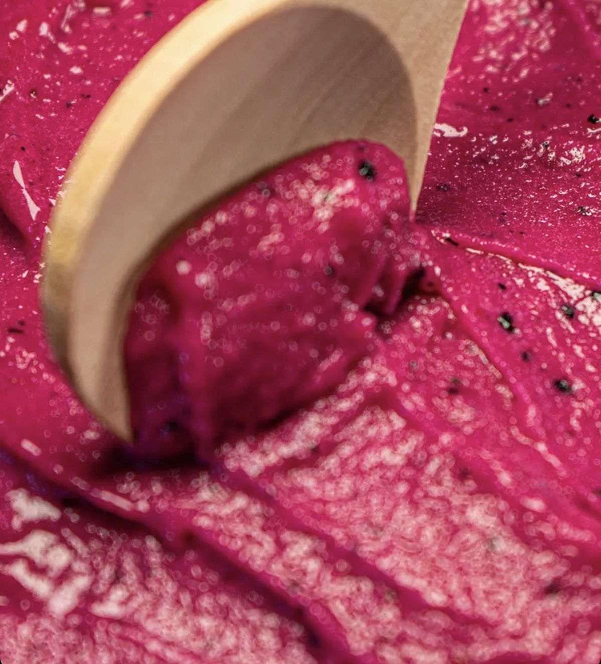 Cremige Textur des Pitaya-Sorbets mit Drachenfrucht-Kernen, Nahaufnahme mit Holzlöffel
